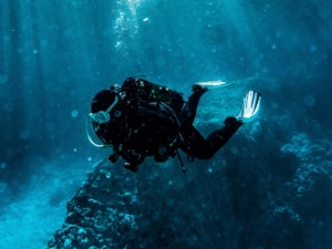 Scuba instructor guiding a student through clear blue waters near Santorini’s volcanic reef.
